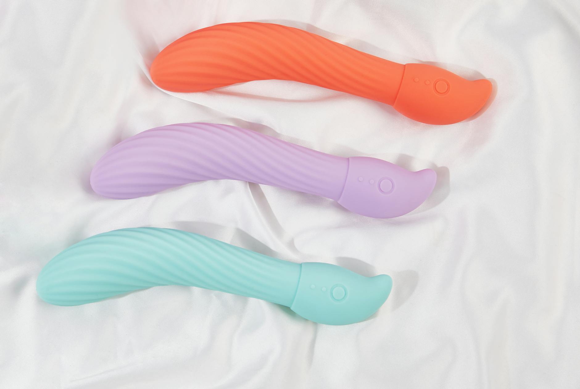 Three colorful suction vibrators arranged on white fabric, showing smooth modern design for first-time users.