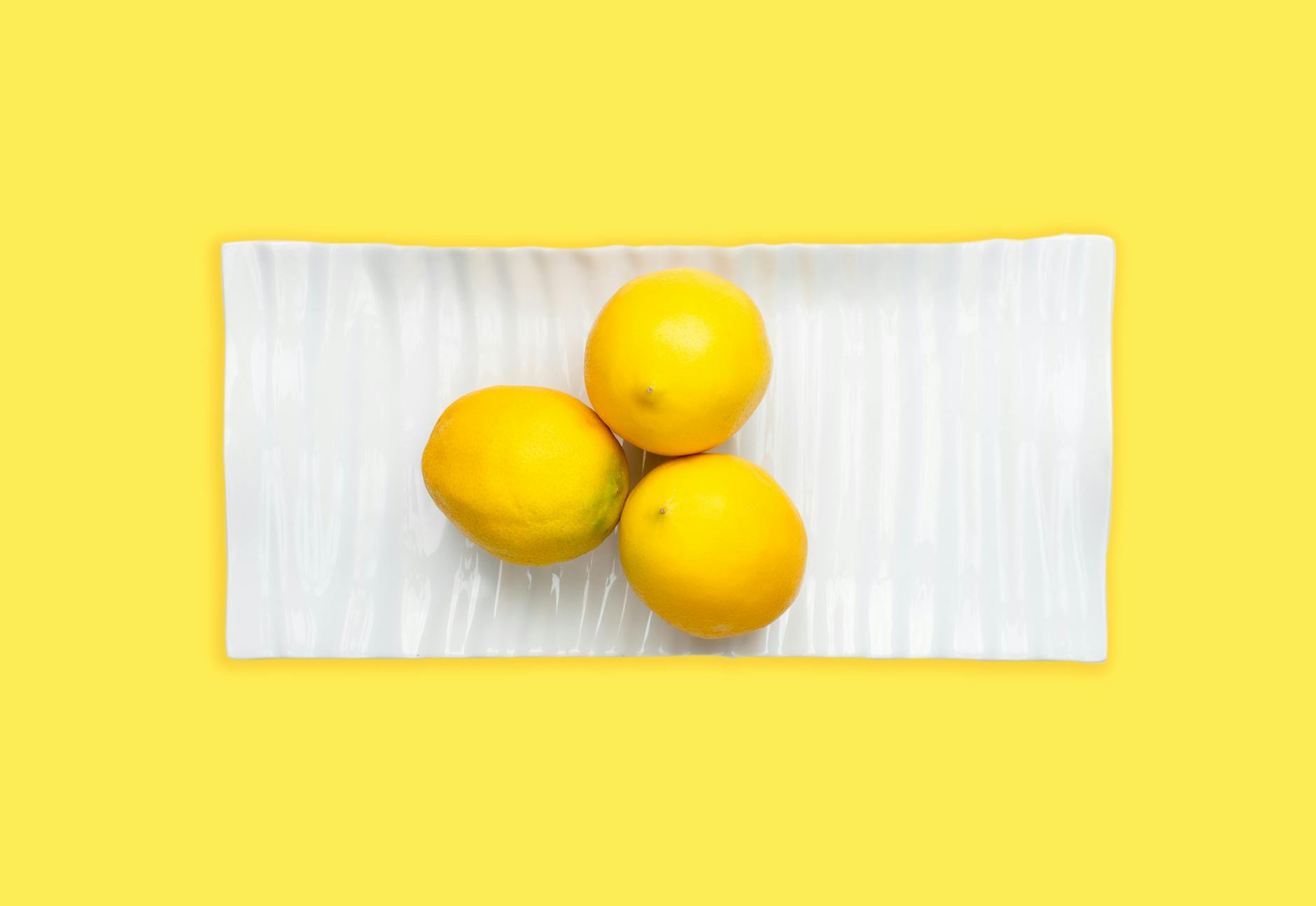Fresh lemons arranged on white plate with vibrant yellow background