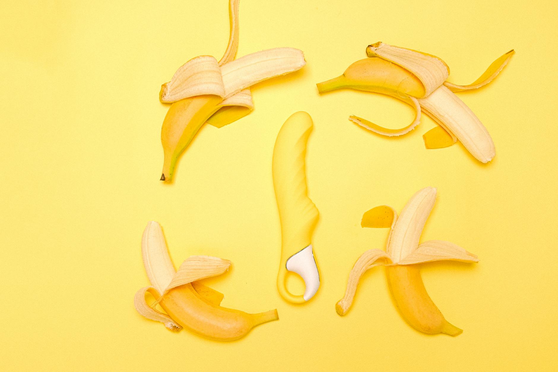 Yellow silicone vibrator surrounded by fresh lemons on a bright yellow background