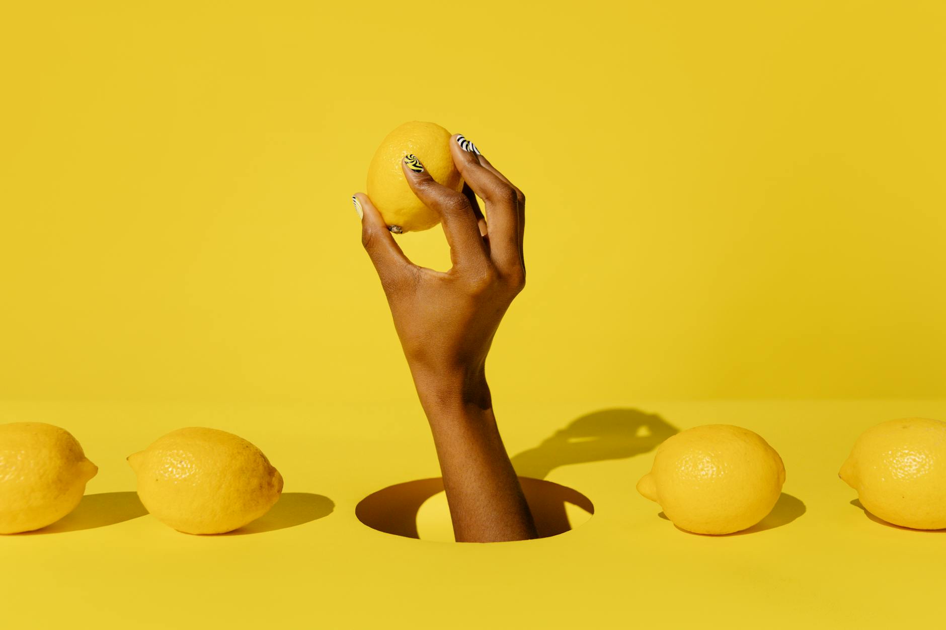 Hand holding a fresh lemon on a bright yellow background, symbolizing the refreshed sensation from Lemon Vibrator technology
