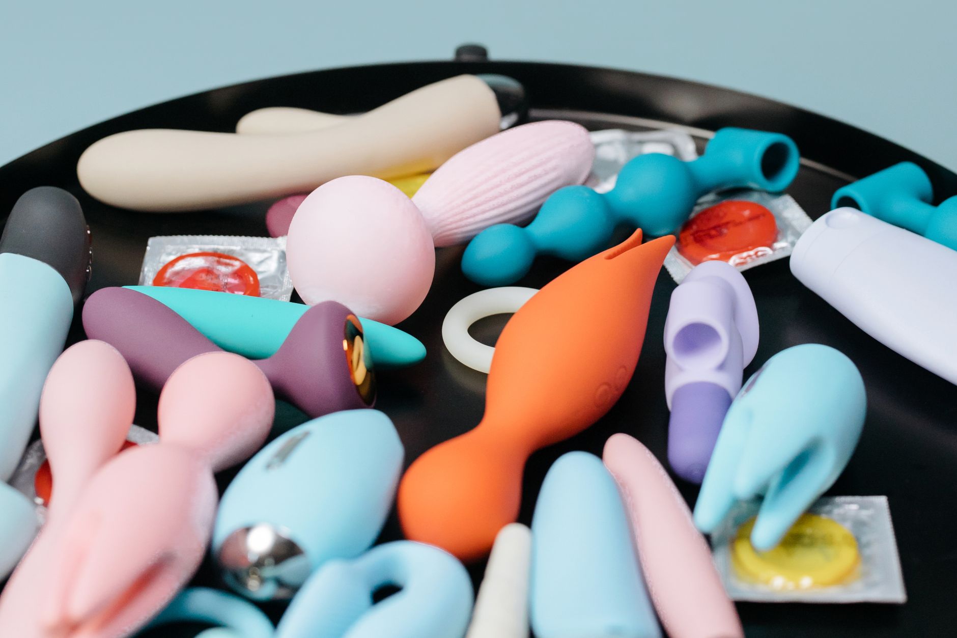 A woman with eyeglasses holds two colorful vibrators, representing the overwhelming array of pleasure options available to modern users.