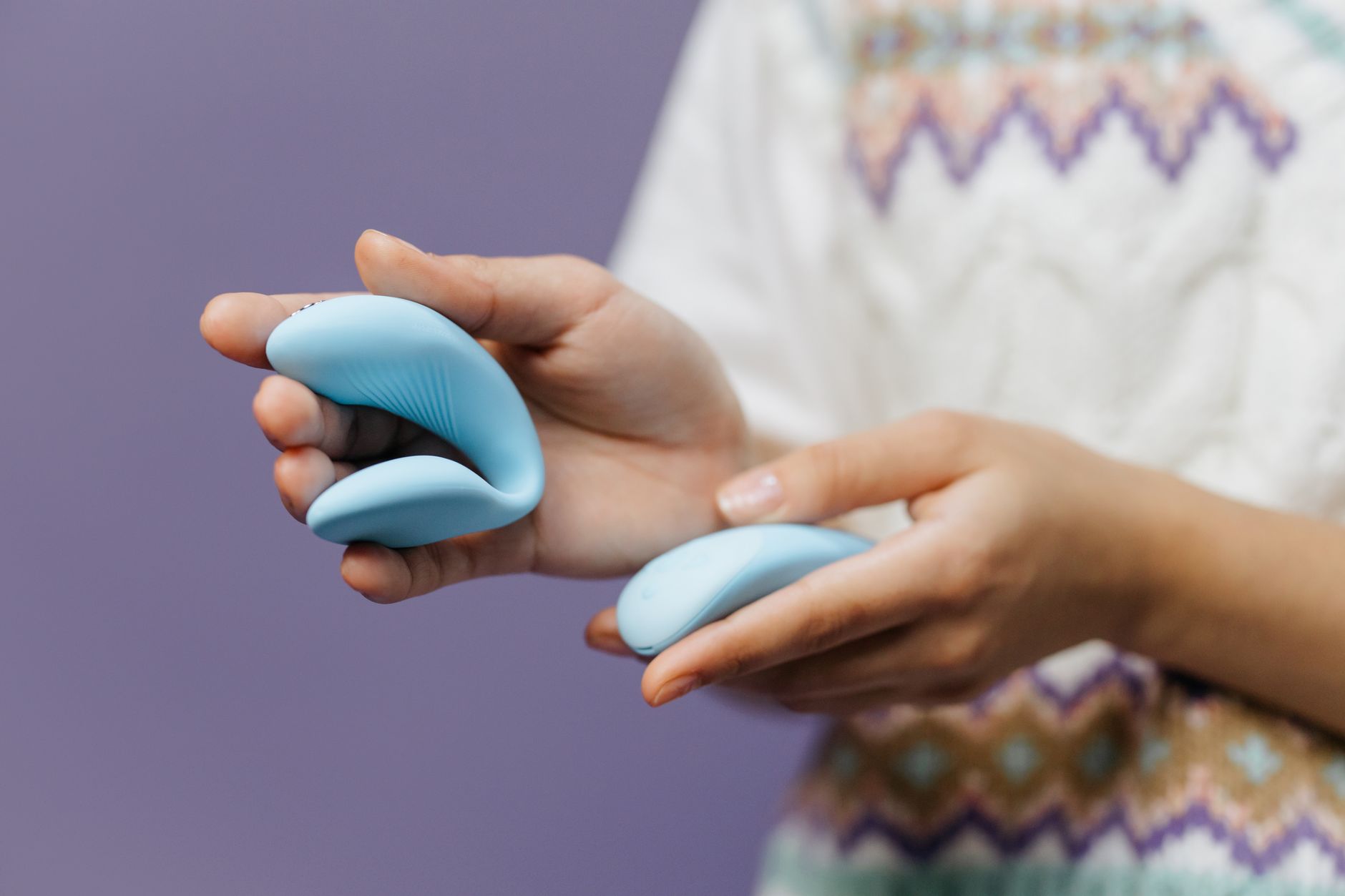 Close-up of hands holding a sleek vibrator against a purple background, showcasing clitoral suction technique