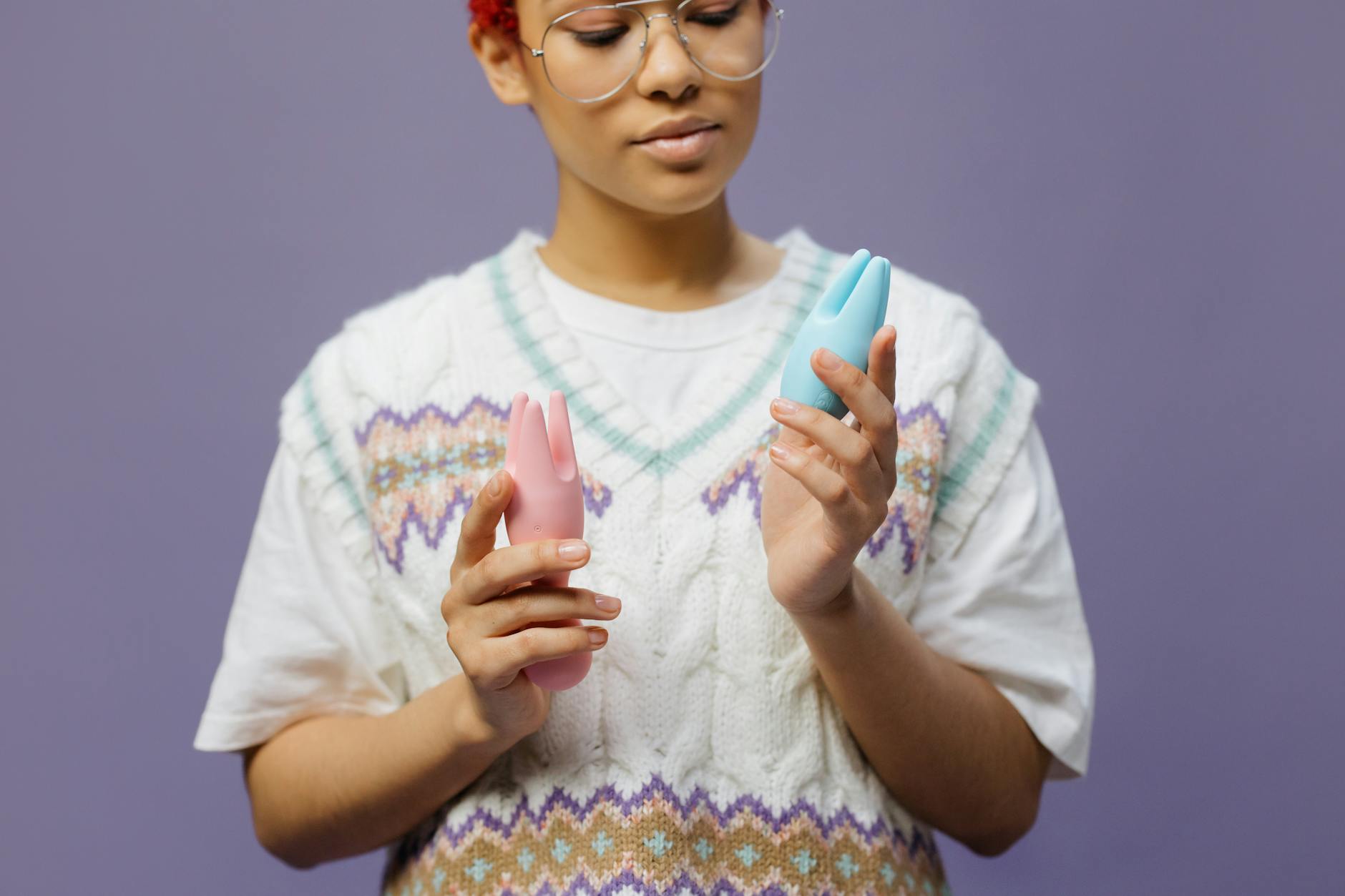 Woman holding blue and pink silicone clitoral vibrators in contemplative moment