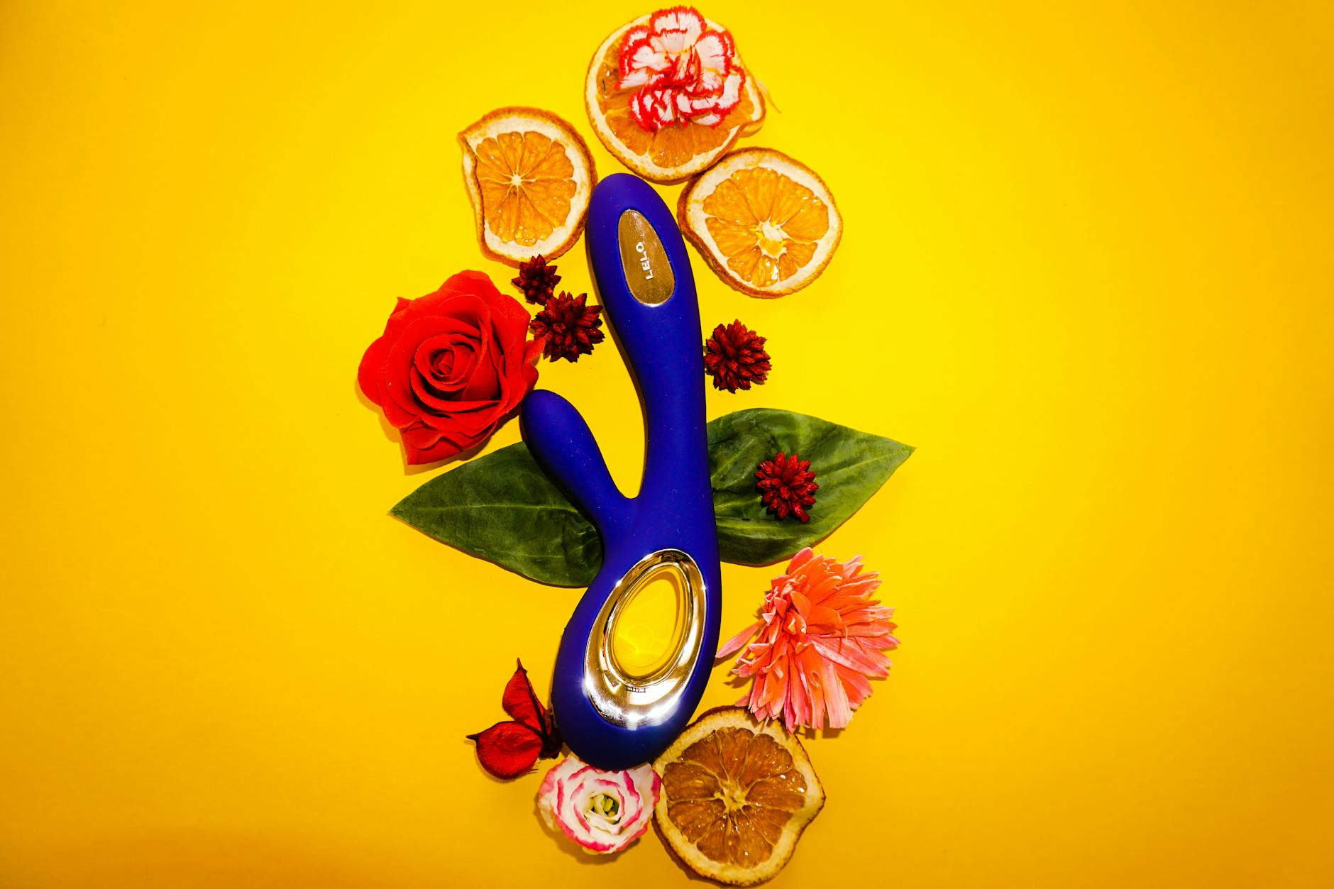 A blue lemon vibrator surrounded by flowers and citrus slices on a yellow background