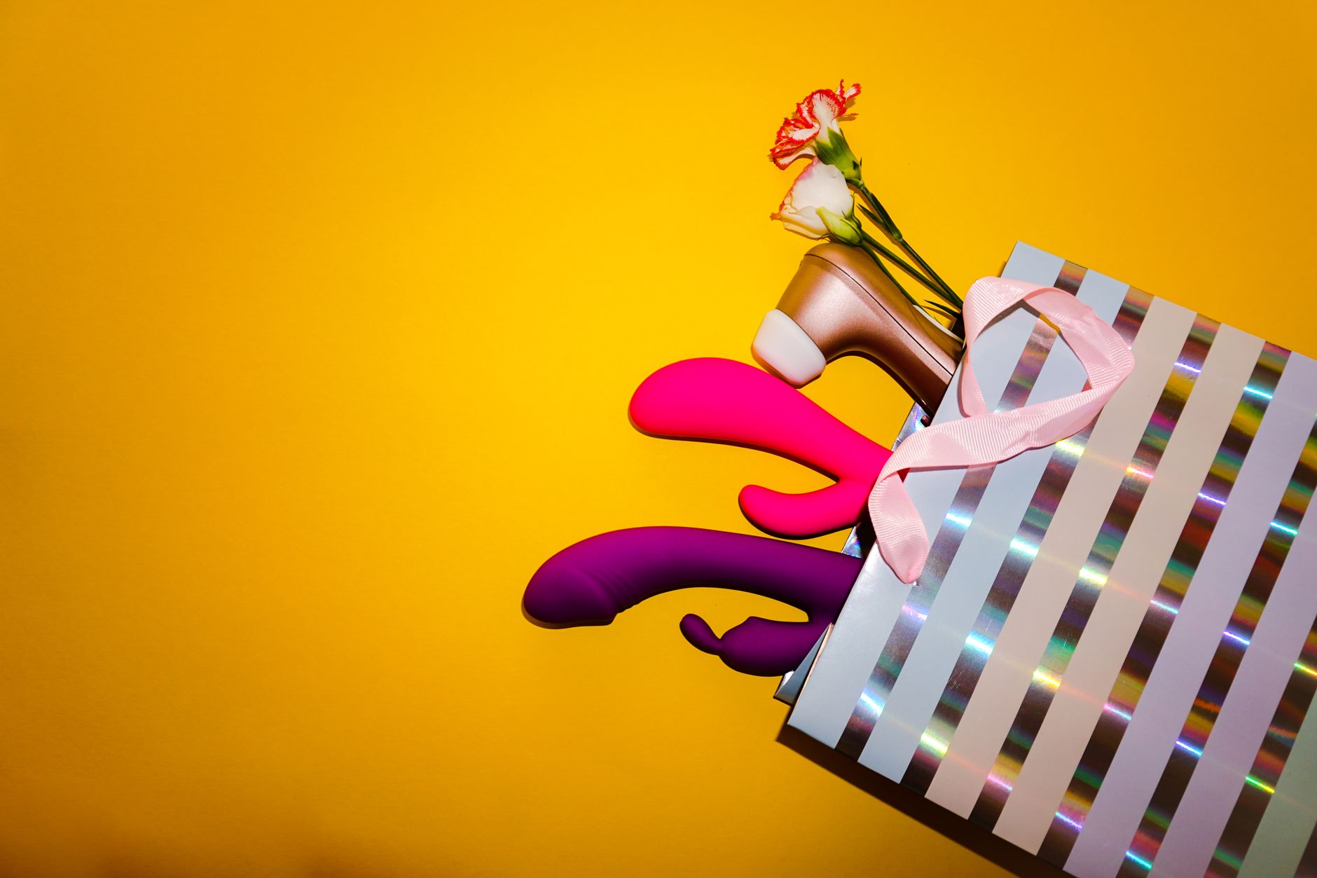 Close-up of a hand holding an orange vibrator against a minimalistic purple backdrop, showcasing modern sensuality and intentional pleasure.
