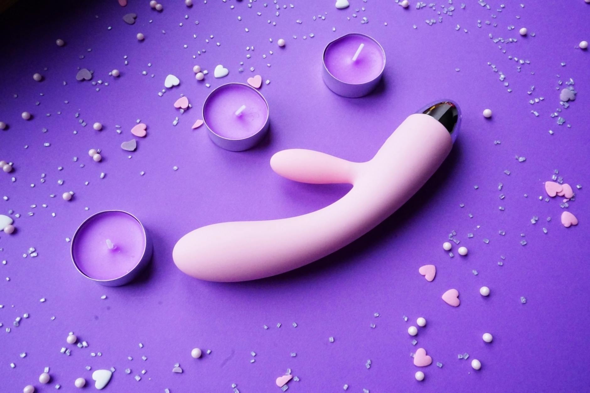 A pink lemon vibrator on a purple background with heart confetti and candles for solo pleasure.