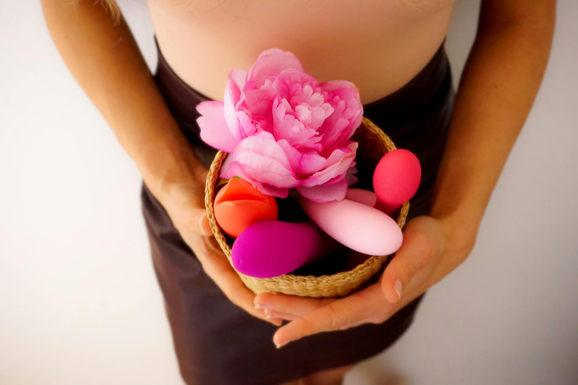 A person's hands holding a sleek vibrator against a warm purple background, representing intimate solo and partnered exploration
